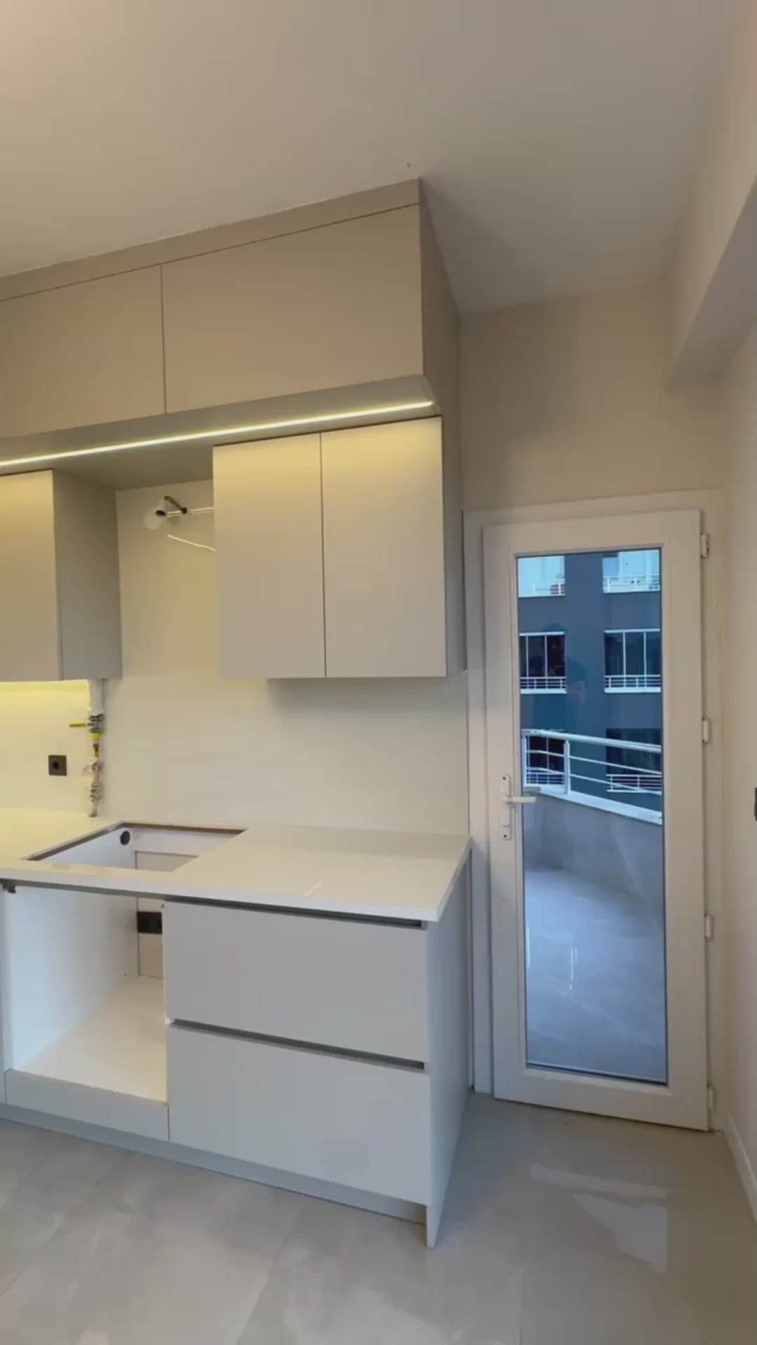 Minimalist beyaz mutfak tasarımı, tezgah ve üst dolaplar, cam kapı ile balkon, LED ışıklı modern mutfak mebeli, yeni inşaat
