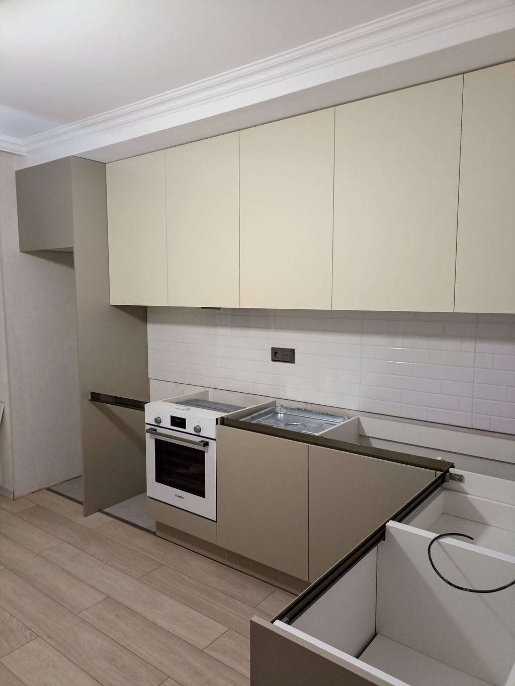 Quraşdırma mərhələsində bej L-formalı mətbəx mebeli və ağ Bosch soba